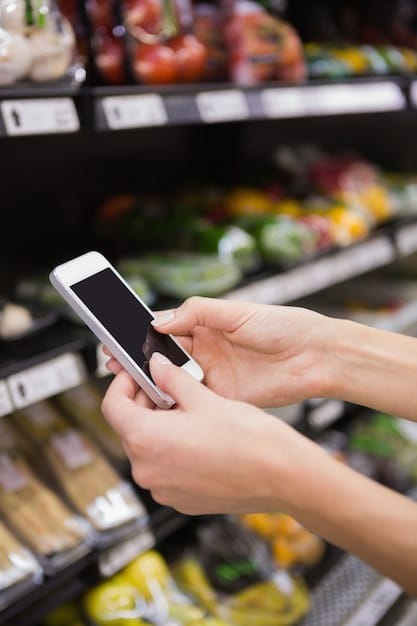 A person's hands using a smartphone app to clip digital coupons while standing in a grocery store aisle. The background shows blurred shelves filled with various grocery products.