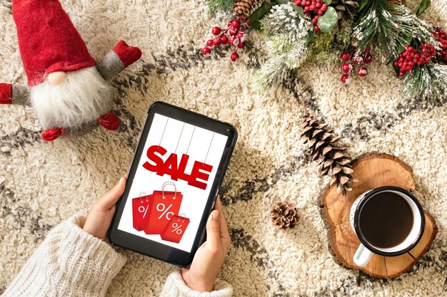 A person using a smartphone to browse a coupon app, with various deals and discounts displayed on the screen. The setting is a cozy living room with holiday decorations in the background.
