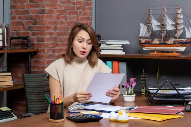 A teacher sits at her desk, organizing receipts and invoices with a calculator in front of her. A laptop is open, displaying a tax form.
