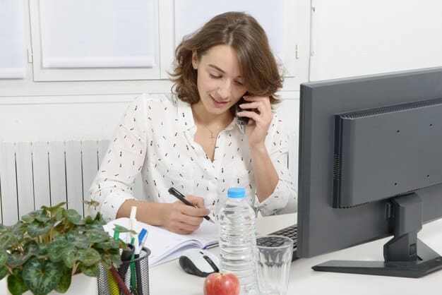 A person sitting at a desk, confidently talking on the phone while looking at notes and a computer screen displaying price comparisons and competitor analysis.