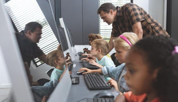 A teacher instructing a small group of students on coding using individual laptops, emphasizing practical digital skill development.