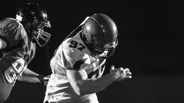 A dynamic shot of a college football quarterback mid-throw, showing intense focus and athletic form, with receiver clearly signaled and open space on the field, conveying effective offensive strategy.