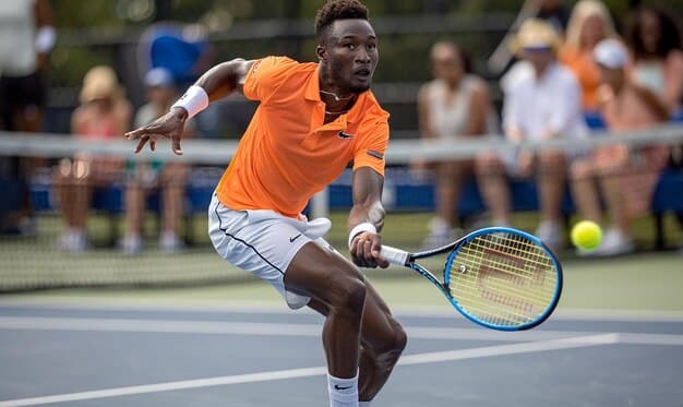 A dynamic action shot of Carlos Alcaraz hitting a forehand, mid-air, with intensity on a hard court during a Grand Slam match.