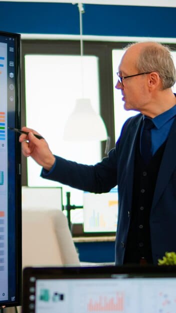 A corporate executive in a modern office, thoughtfully reviewing a digital dashboard displaying various metrics related to a distributed workforce, emphasizing data-driven decision-making in human resources. The background shows blurred office activity, suggesting a dynamic environment.