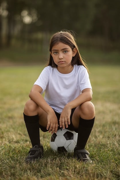 A young girl, about 10 years old, with determination on her face, kicking a soccer ball in a vibrant green field, surrounded by other children in motion, suggesting an active and engaging training session.