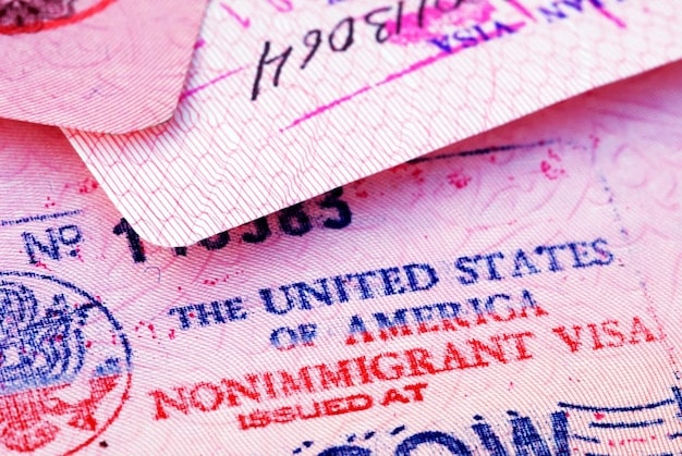 A close-up of a US passport with visa stamps from multiple countries. The focus is on the stamps, symbolizing the complex process of legal immigration. There's a sense of anticipation and possibility conveyed, but also a hint of the challenges associated with US Immigration Policy Changes: What New Regulations Mean for Families and Businesses in 2025